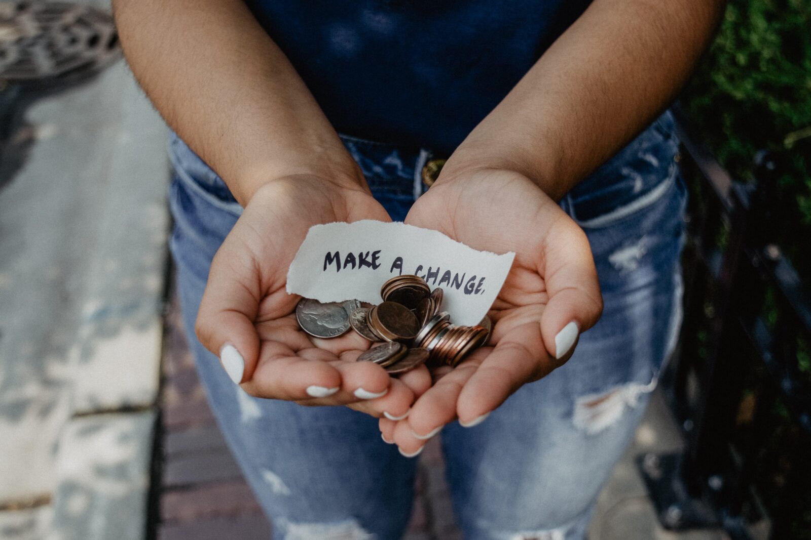 Photo of a woman's hands cupped together holding a pile of change with a slip of paper that says "make a change"